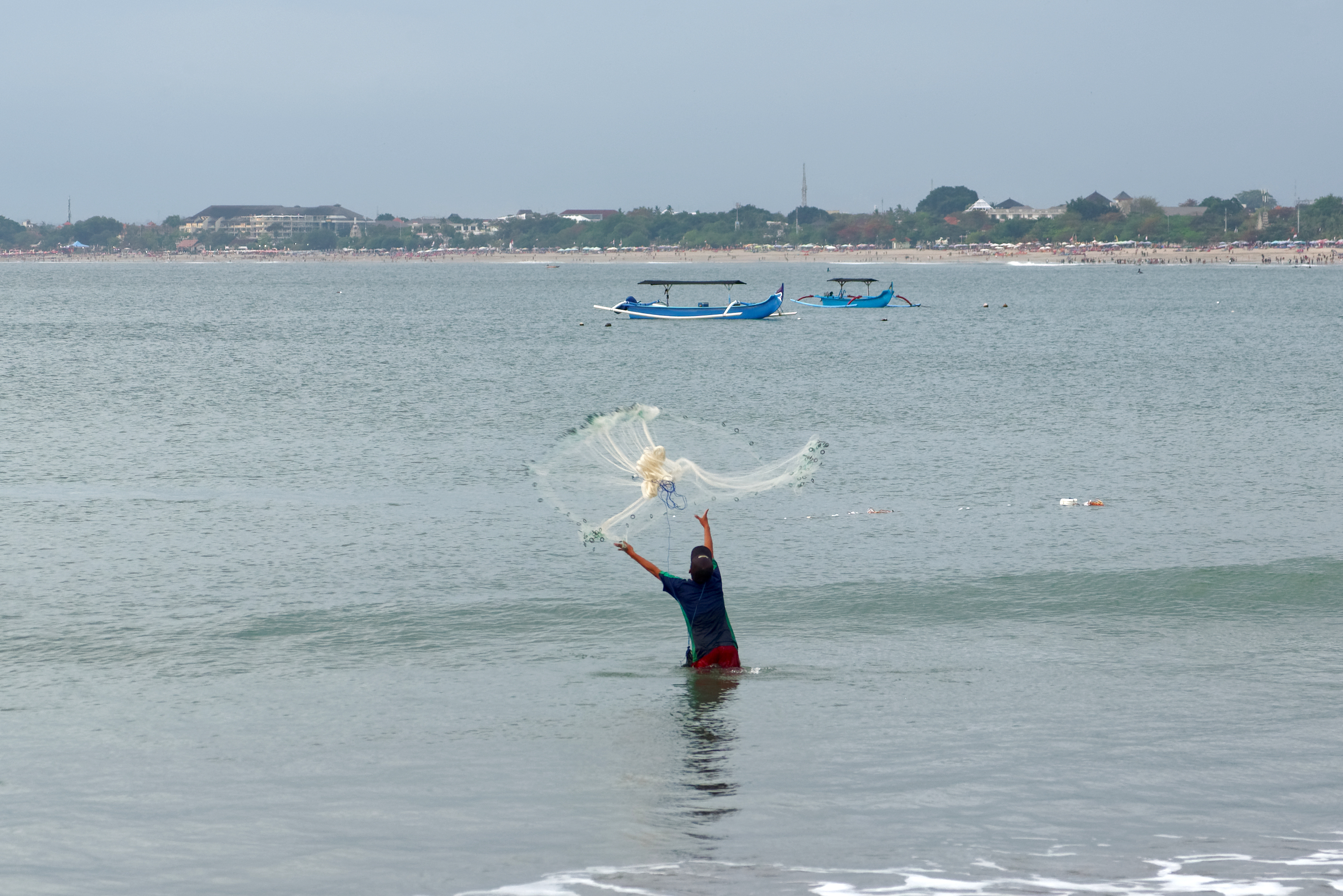 A fisherman casting a net in shallow water at Kuta Beach, Bali, in August 2022